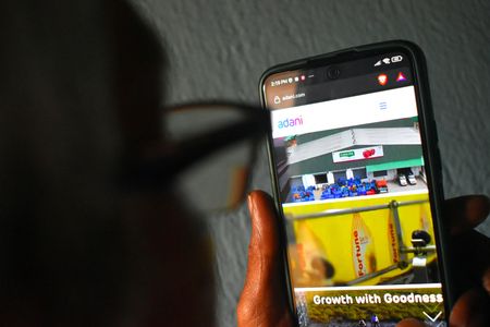 A person checking the Adani website on his mobile. Adani group of companies have lost market capitalization of over Rs 7 lakh crore after a US-based Hindenburg Research report accused the group of “brazen stock manipulation and accounting fraud.” Bank stocks were also hit following the plunge in Adani stocks.