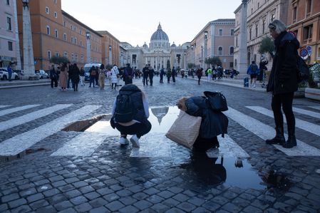 Tourists take pictures of reflection of St. Peter's Dome in a puddle on Via della Conciliazione.