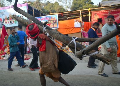 A physically challenged pilgrim carrying wood on his shoulder walking towards his tent on Gangasgara transits camp.