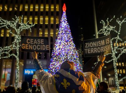 A pro-Palistine protester holds up signs during a rally at the News Corp. building near the Rockefeller tree lighting. The rally comes as the initial four-day truce between Israel and Hamas was extended by two days pausing the seven weeks of warfare that has killed thousands in Gaza as a result of the October 7th Hamas attack in Israel.