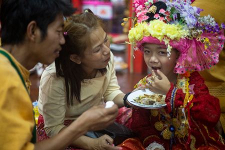 The parents are feeding their son the last meal before the ordination.