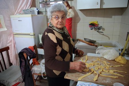 Pagani, Salerno, Italy - April 14, 2023:Old women make party food. During the days of the feast of the Madonna delle Galline , in the historic center and around the Sanctuary of the Madonna, dances are held to the sound of chestnuts and tammorre. In the alleys of the old town the elderly women prepare the food of the festival : noodles, roasted artichokes and other typical products of the festival. Young people linked to tradition prepare in their homes the so-called "Tosello", small corner of the house with the statue of the Madonna and the products of the earth that are offered to the passage in procession of the statue of the Madonna.