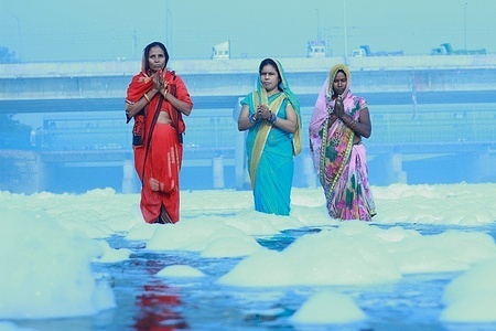 Indian women praying in front of the Sun god in the polluted Yamuna Waters.