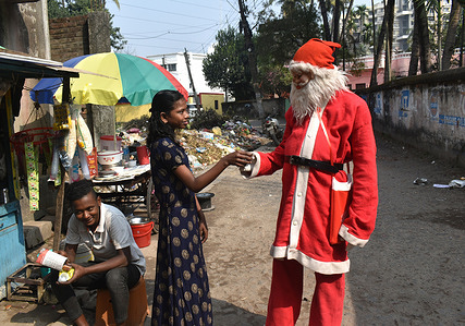A girl giving a tea cup to Krishna Naskar, who dressed up like a Santa Clause. Krishna Naskar, 18, a Bahurupi artist dressed up like a Santa Clause on the occasion of Christmas in Kolkata.