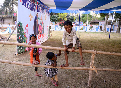Children are come from different distant Villages to celebrate Holy Christmas in a small and only church in the area, and play in front of a large Jesus Christ photo without a mask during the threat of Omicron (Covid-19) in India at Haulia, West Bengal.