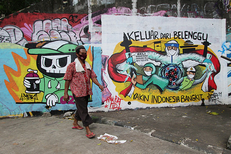 Hasan Basri, 55, walks through a mural that reads encouraging residents to rise up against Covid-19 in the Bidara Cina Village area, Jatinegara, East Jakarta, Saturday, January 1, 2022. The spread of Covid 19, the Omicron variant, is still a threat to people around the world. The number of Covid-19 cases of the Omicron variant in Indonesia has increased by 68 people. This brings the total cases, which were first detected in South Africa, to 136 people. The addition of 68 Omicron cases came from overseas travelers. Of the 68 new cases, 11 of them are foreign nationals.