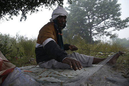 A fisherman from Bengal preparing nets for fishing on the banks of river Yamuna during winter.