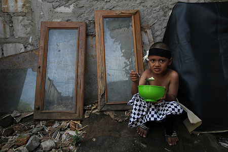 A student wearing traditional clothes from the Balinese area having breakfast after participating in a flag ceremony to commemorate the Birthday of Pancasila, at the Kartini Emergency School yard, under the Ancol Toll Road, Jakarta, Indonesia. The Kartini Emergency School is managed by twin brothers Rossy and Ryan, accommodating underprivileged students from various groups without being charged a penny. Even though their school is located on the outskirts of under the toll road and train tracks, the enthusiasm of the children involved in the series of events was full of meaning in their traditional clothes. The birthday of Pancasila is celebrated nationally every June 1. Pancasila is the basis of the Indonesian state which is the foundation of the founding of the Indonesian state.