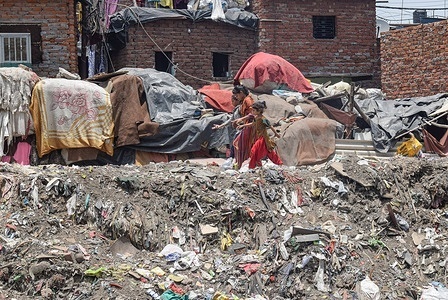 People walk through a dump full of garbage at Taimoor Nagar on the eve of World Environment Day in New Delhi.