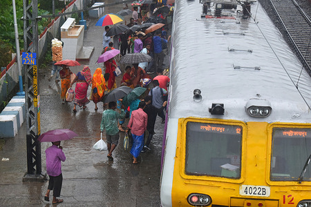 People board a train at a railway station during rains in the outskirts of Kolkata.