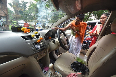 A priest is performing puja on a passenger car during Vishwakarma Puja festival. Lord Vishwakarm is a Hindu god, the divine architect and considered as creator of the world who protects vehicles from various calamities.
