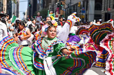 Participants are performing traditional folklore dance along Madison Avenue, New York City during the Mexican Day Parade.