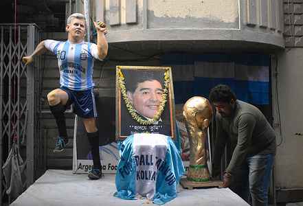 A person places a Football World cup Trophy replica next to a picture of Argentina's soccer Late Maradona and a model of Lionel Messi during the FIFA World cup 2022 in Kolkata.
