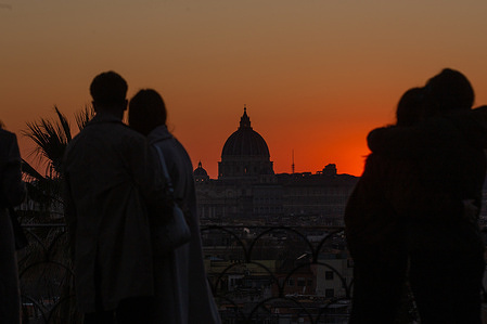 Couples watch the sunset from the promenade near Pincio Terrace on Valentine's Day, with St. Peter's Dome in the background.