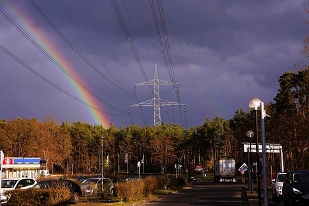 After the rain, a large rainbow can be seen in the sky above the high-voltage lines in front of the trading center in Strausberg in Märkisch Oderland.
