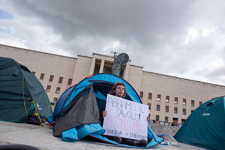 A student sitting in a tent in front of the rectorate of the University of Rome "La Sapienza" shows a banner relating to the public assembly that will take place tomorrow afternoon, to protest against the high rents of the rooms