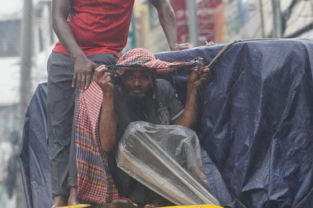 A worker covers his head with a gamchha (a traditional cloth) amid light drizzle rain in Dhaka.