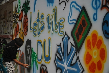 A student draws a spray painting on a board as they start a music festival on the campus of Dhaka University.