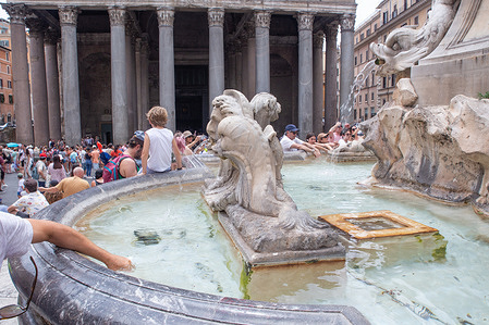 Tourists immerse their hands in the fountain of the Pantheon in Rome on a hot summer day