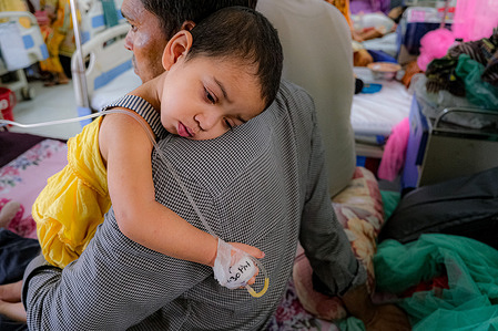 A dengue affected child is resting on her father's shoulder.