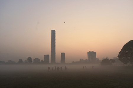 People are walking through a field on a foggy winter morning in Kolkata.