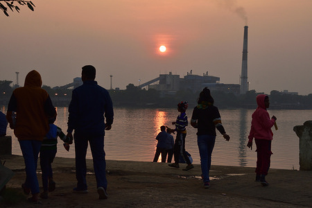 People observing the sunset over Kolkata skyline on the winter solstice day in the northern hemisphere from the AJC Bose Indian Botanic Garden adjacent ghat of the Ganges in Howrah.