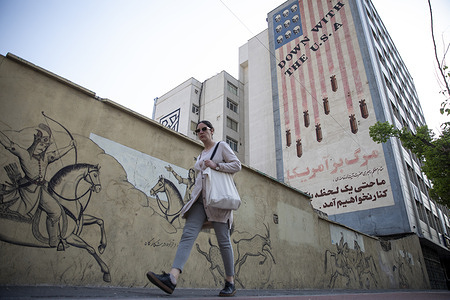 A woman walks past a mural reading 'Down With The U.S.A.' in Tehran, Iran, on Sunday, April 14, 2024. Israel on Sunday hailed its air defenses in the face of an unprecedented attack by Iran, saying the systems thwarted 99% of the more than 300 drones and missiles launched toward its territory.